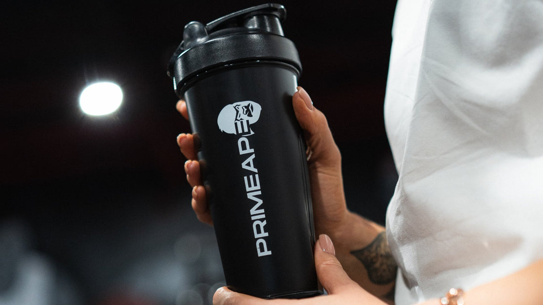 person holding a black Prime Ape shaker bottle, an essential gym accessory for staying hydrated and mixing protein shakes during workouts.