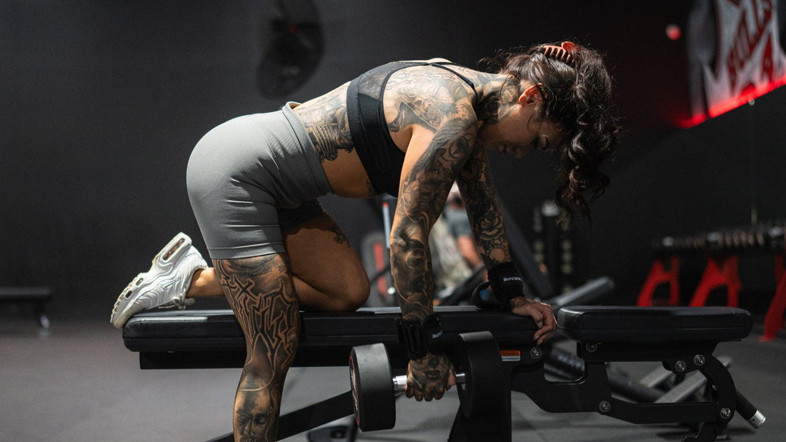 A woman performing a dumbbell row in a gym while wearing lifting straps, showcasing their use for improved grip and support during strength training.