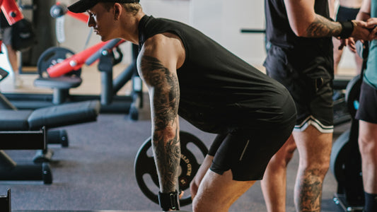 A person performing a deadlift at the gym, focusing on proper form, with tattoos visible, emphasizing gym fitness and strength training.