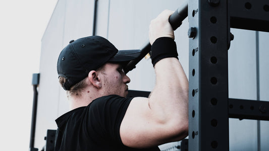Side view of a person wearing a black cap and performing a pull-up on an outdoor gym rack, with a focus on upper body strength and muscle engagement