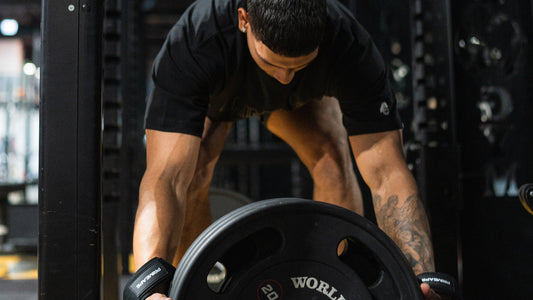 Muscular man in a black T-shirt using an overhand grip to lift a heavy weight plate in a gym, demonstrating strength and focus during a workout
