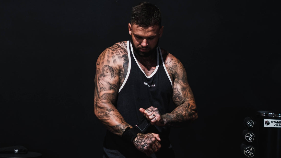 Man preparing for a workout by adjusting weightlifting straps, showcasing detailed tattoos on his muscular arms