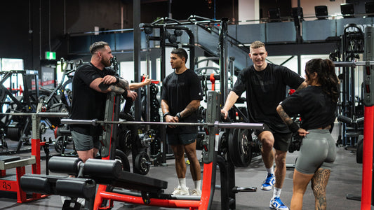 Group of gym-goers engaging in a casual conversation at a modern fitness facility, surrounded by weightlifting equipment and gym machines.
