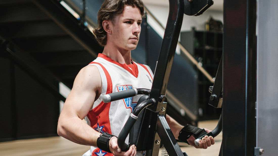 Young man in a white and red basketball jersey performing a chest press exercise on a machine at the gym, focusing on upper body strength.