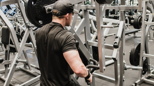 Man performing strength training on gym equipment, focusing on back and arm muscles, in a fully equipped fitness centre.